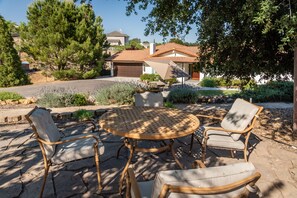 A patio with a round table and four chairs, surrounded by a landscaped garden with various plants and trees.