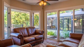 A spacious living area with a brown leather sofa, a patterned rug, and large glass doors leading to an outdoor patio.