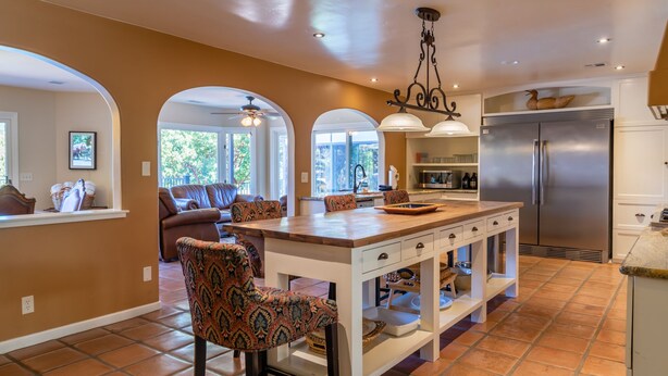 A spacious kitchen with a central island, a refrigerator, and a dining area with patterned chairs.