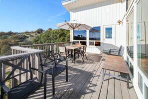 Une terrasse en bois aménagée avec du mobilier d’extérieur, notamment une table et des chaises, ainsi qu’un grand parasol.