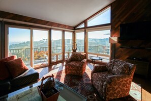 A spacious living room with large windows, a comfortable sofa, patterned armchairs, and a small table with decorative items. - Vineyard Views + Deck | Near Downtown Paso | Peachy Canyon Place (Paso Robles)