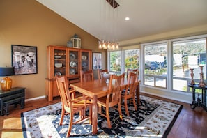 Un comedor con mesa y sillas de madera, un armario con puertas de vidrio y un ventanal con vistas al exterior.