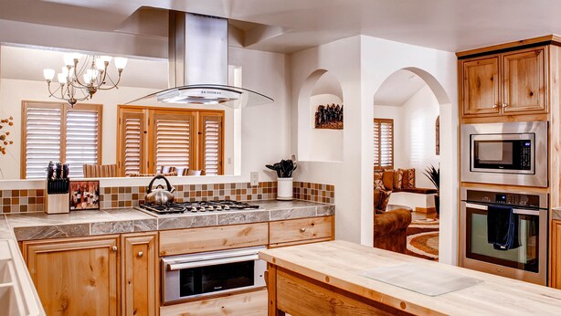 A kitchen with wooden cabinets, a stainless steel range hood, a microwave, and a built-in oven.