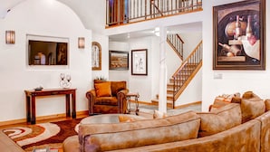A spacious living area with a large brown leather sofa, a wooden coffee table, and a fireplace. A staircase leads to an upper level with a balcony.
