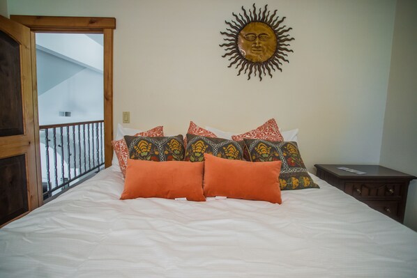 Un dormitorio con una cama, almohadas estampadas, cabecera de madera, mesita de noche y un adorno de sol montado en la pared.