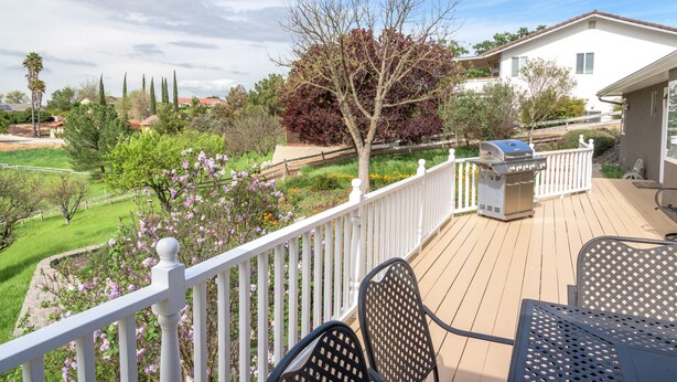 Una terraza con mobiliario exterior, una parrilla y vistas a un jardín ajardinado con árboles y flores.