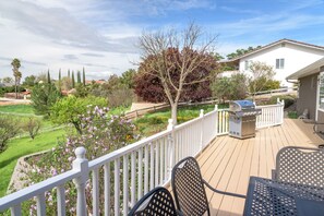 A deck with outdoor furniture, a barbecue grill, and a view of a landscaped garden with trees and flowers.
