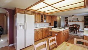 Una cocina con armarios de madera, un refrigerador, un microondas y un comedor con una mesa y sillas.