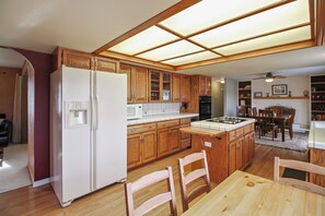 A kitchen with wooden cabinets, a refrigerator, a microwave, and a dining area with a table and chairs. - Private Deck + Hillside Views | Paso Robles Wine Country | COF House (Paso Robles)