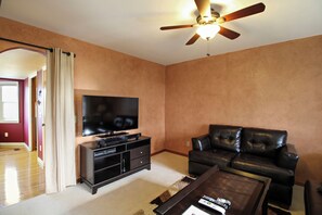 A living room with a flat-screen TV, a leather sofa, a coffee table, and a ceiling fan. - Private Deck + Hillside Views | Paso Robles Wine Country | COF House (Paso Robles)