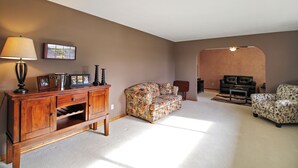 Ein Wohnzimmer mit einem Holzkabinett, einem Blumensofa, einem Ledersessel und einem Teppich.