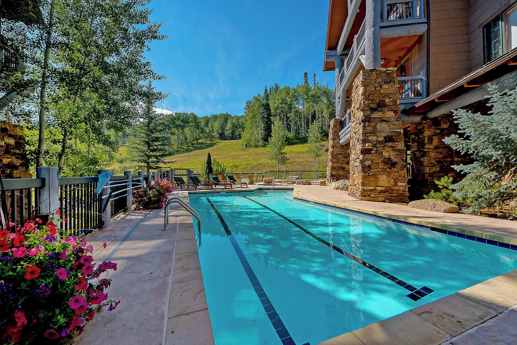 A swimming pool with a stone wall and a view of a forested hillside.