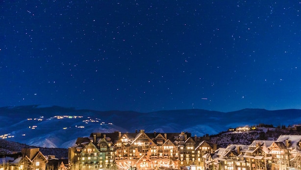 Ein verschneites Dorf bei Nacht mit beleuchteten Häusern und einem Berg im Hintergrund.