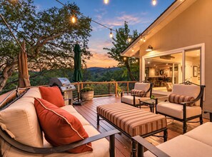 An outdoor deck with a grill, seating area, and string lights.
