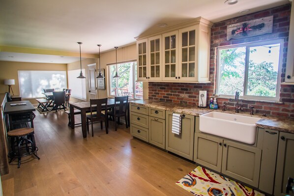 Una cocina con armarios de madera, un ventanal grande y una zona de comedor con mesa y sillas.