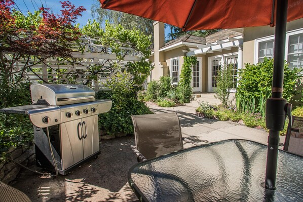 Une terrasse extérieure avec un barbecue, une table en verre et une chaise.