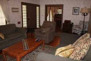 A living room with a sofa, armchair, and a coffee table with remote controls. - Historic Craftsman + Garden Patio | Walk to Downtown | Jany House Downtown (Paso Robles)