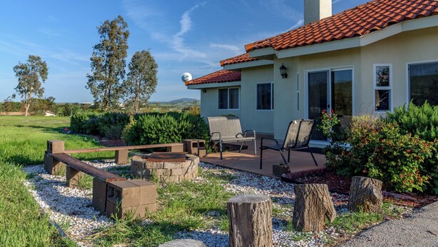 A house with a red-tiled roof, a patio with outdoor furniture, and a garden with various plants and a wooden deck. - Vineyard Views + Jetted Tubs | Paso Wine Country | Uvae Vineyard (Paso Robles)