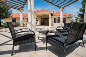 Une terrasse extérieure avec des meubles en osier, une pergola et une maison avec un toit recouvert de tuiles rouges.