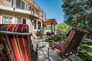 Un espace patio agrémenté de meubles d’extérieur à rayures, d’une pergola et offrant une vue sur une maison dotée d’un balcon.