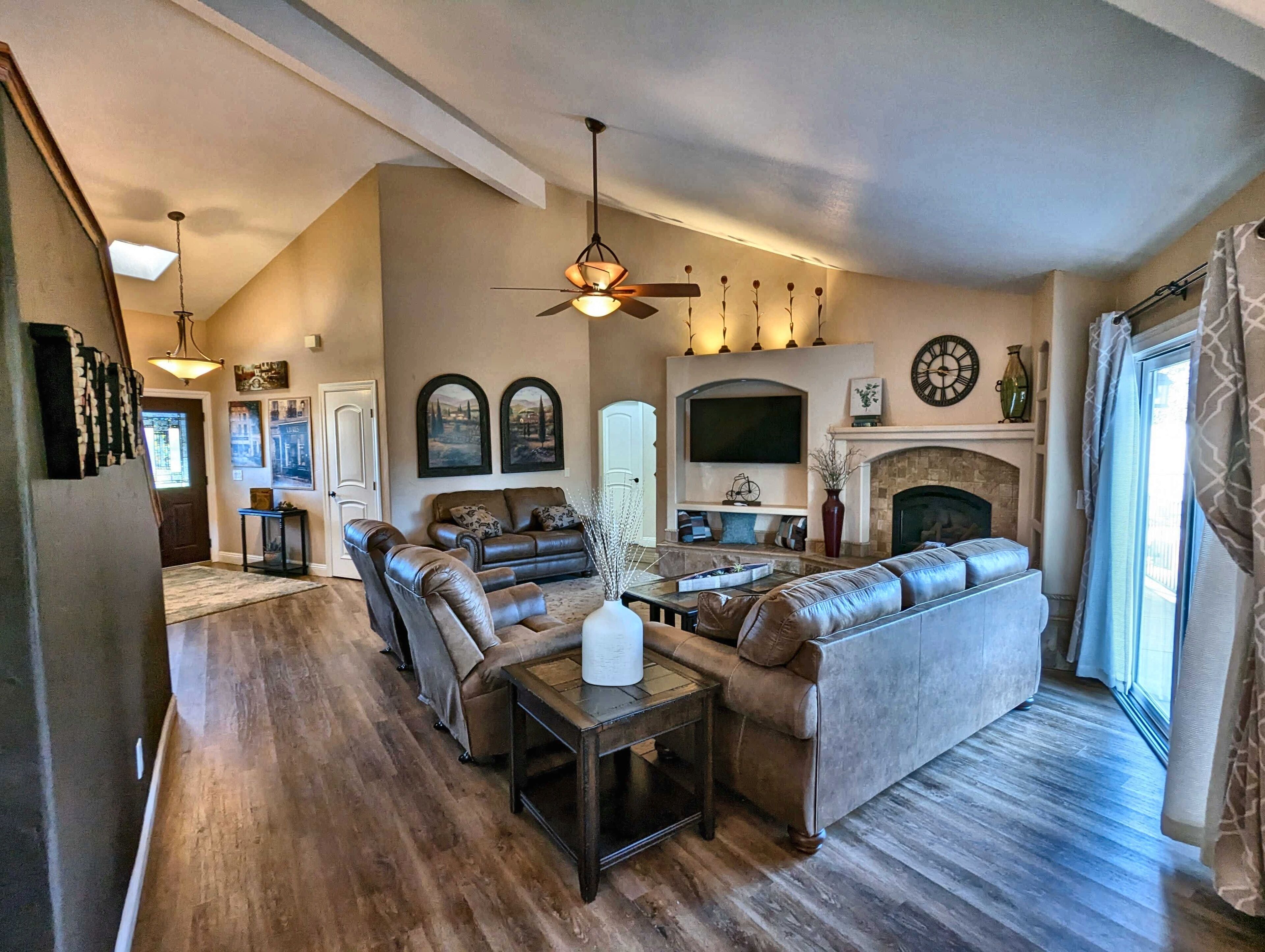 A spacious living room with a fireplace, leather sofas, a coffee table, and a ceiling fan.