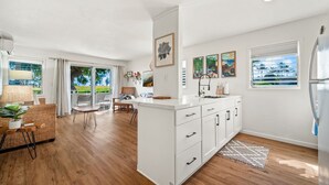 A modern kitchen with white cabinetry, a central island, and a view of greenery outside. - Plantation Hale Suite J8 AC, King Bed, Garden View, Ground Floor, Near Shops (Kapaa)