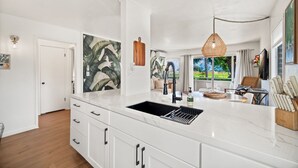 A modern kitchen with white cabinetry, a black sink, and a hanging woven light fixture. - Plantation Hale Suite J8 AC, King Bed, Garden View, Ground Floor, Near Shops (Kapaa)