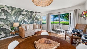 A living room with a large mural, a round wooden table, and a wicker chair. - Plantation Hale Suite J8 AC, King Bed, Garden View, Ground Floor, Near Shops (Kapaa)