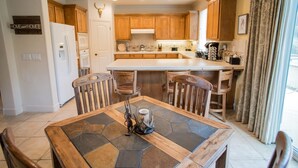 Une cuisine moderne avec des meubles en bois, un îlot central et un coin repas doté d’une table recouverte de carreaux de pierre.
