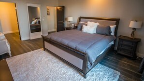 A bedroom with a large bed, bedside tables, a wardrobe, and a door leading to another room.