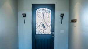 A dark blue door with decorative glass panels and a metal design, flanked by wall-mounted light fixtures.