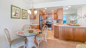 A modern kitchen with wooden cabinets, a glass dining table, and a hanging light fixture.