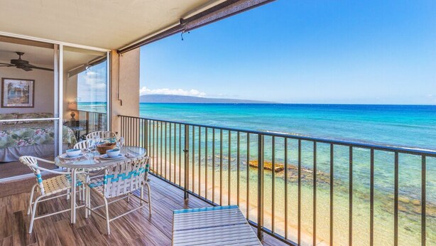 A balcony with a view of the ocean, a table with chairs, and a ceiling fan.