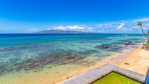 A beach with clear turquoise water, a sandy shore, and a distant mountain.