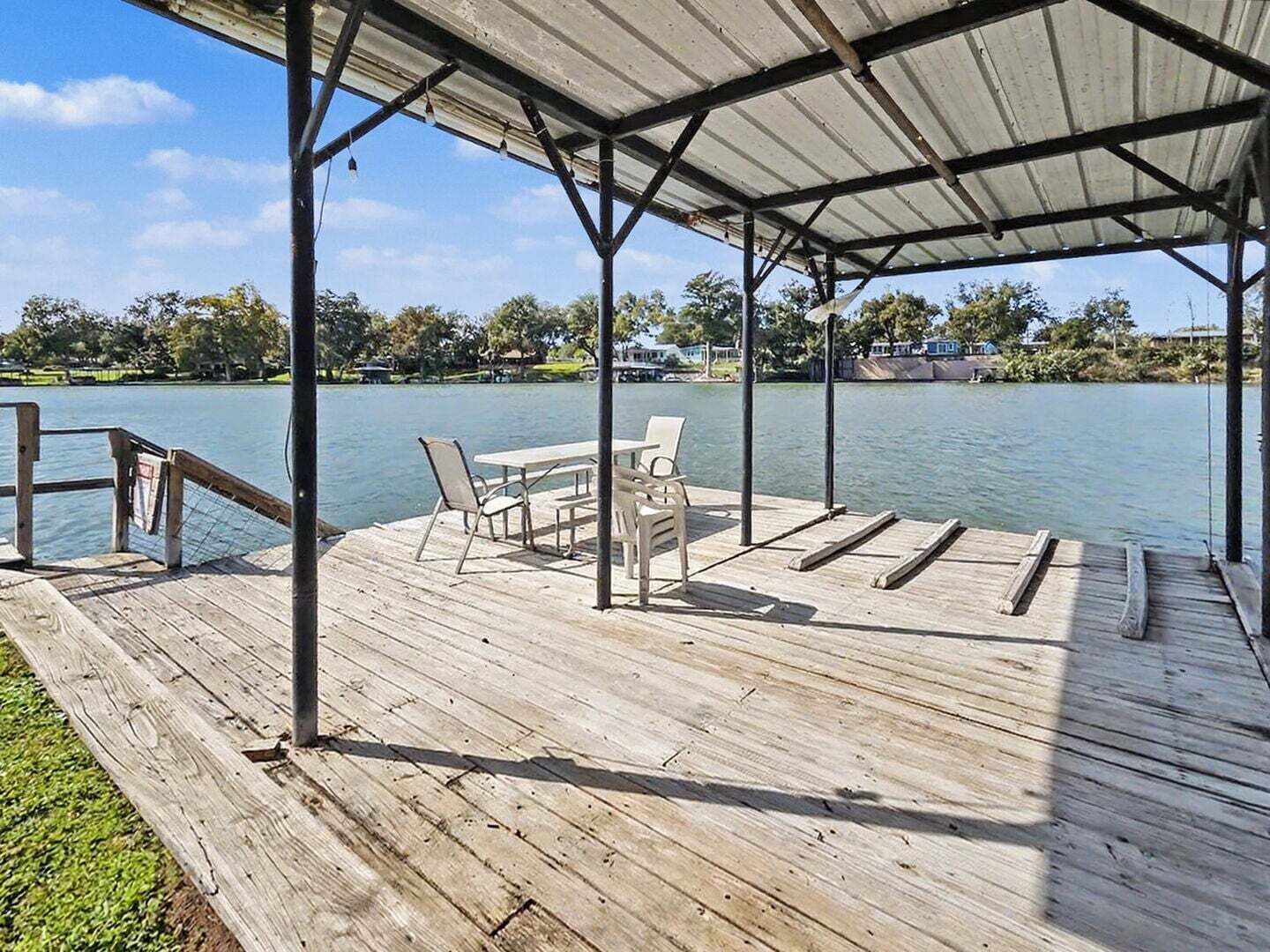 Un muelle de madera con un área de descanso techada, una mesa y sillas que dan a un cuerpo de agua.