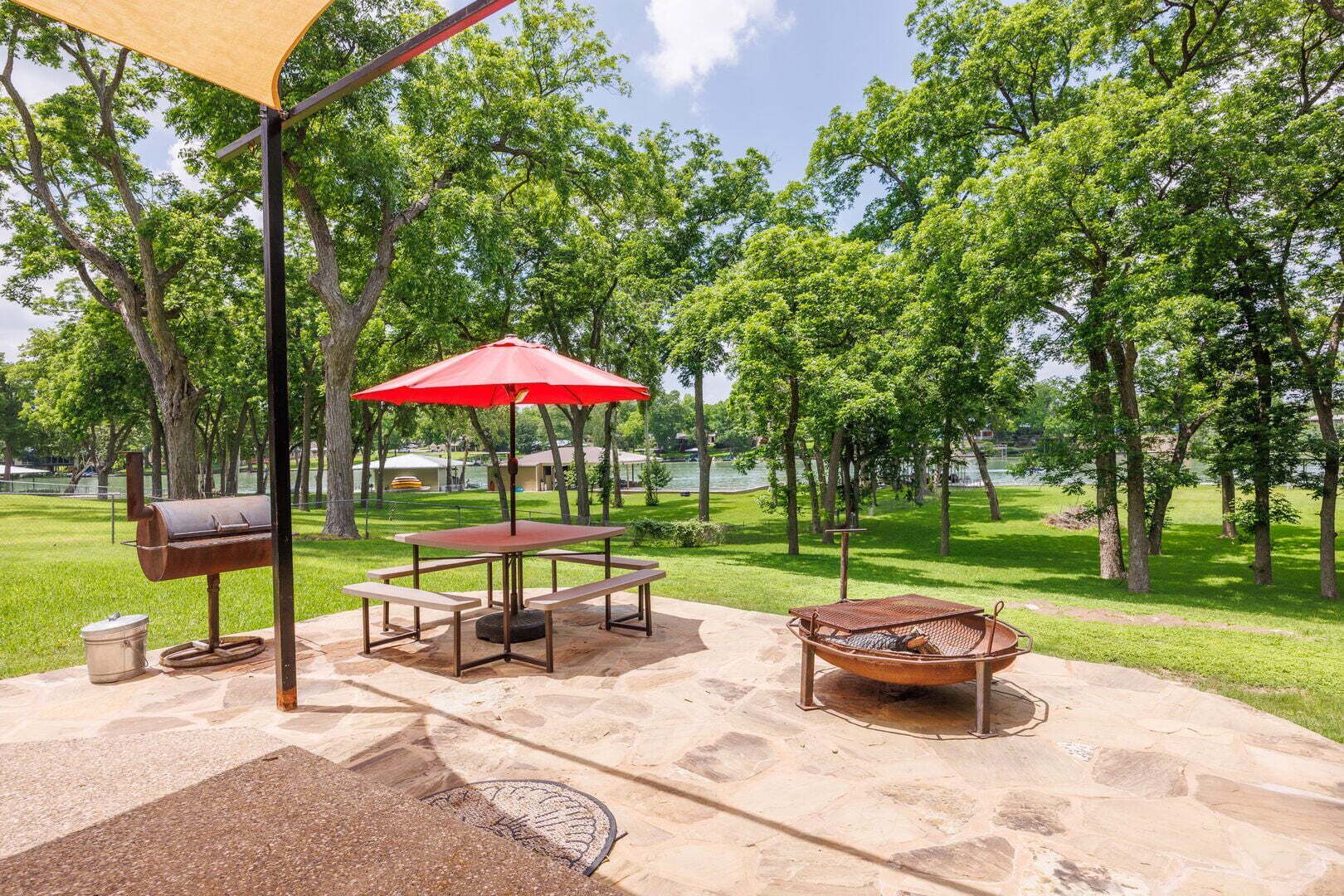 Un patio al aire libre con una parrilla, una mesa de picnic y una sombrilla.