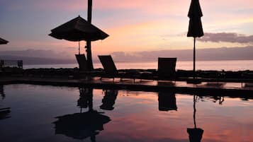 Zona junto a la piscina con sillas de descanso y sombrillas, reflejando una puesta de sol sobre el océano.