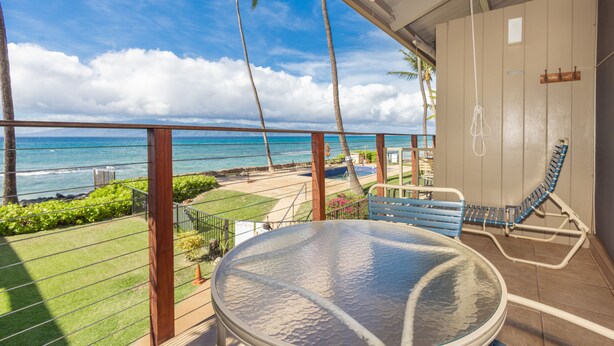 Un balcon avec une table en verre, une chaise bleue et une vue sur l’océan et les palmiers.