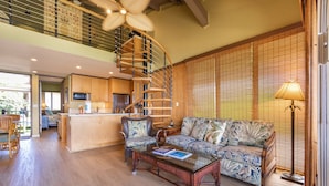 Un vaste espace de vie doté d’un plancher en bois, d’un grand canapé, d’une table basse et d’un escalier en colimaçon menant à un niveau supérieur.