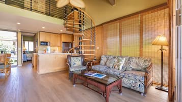 A spacious living area with a wooden floor, a large sofa, a coffee table, and a spiral staircase leading to an upper level.