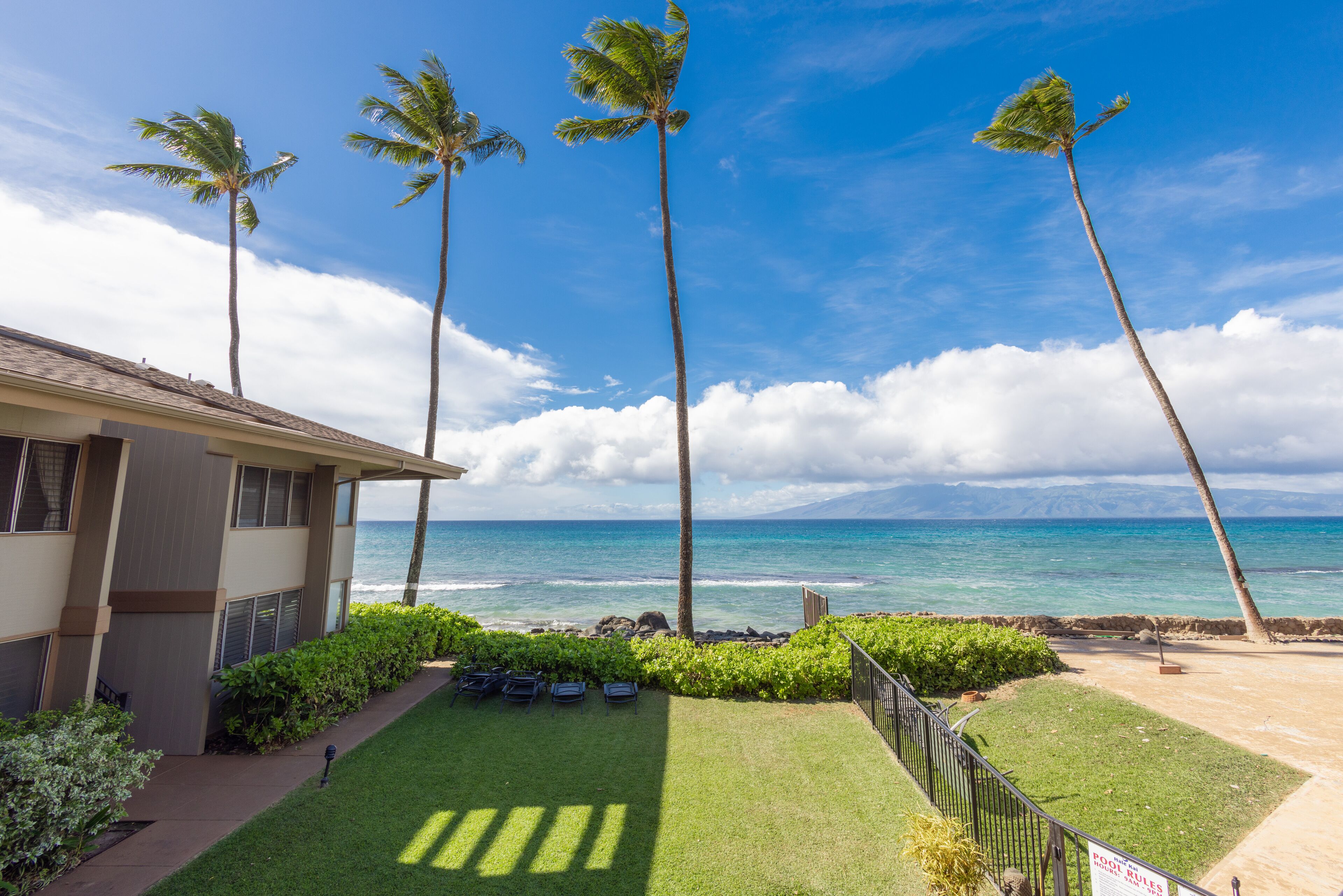 A hotel with a view of the ocean, palm trees, and a well-maintained lawn.