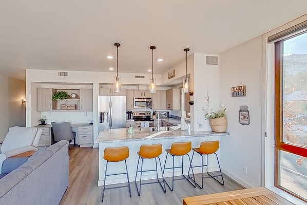 A modern kitchen with a central island, bar stools, and pendant lighting.