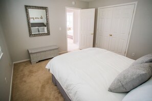 A bedroom with a large bed, a dresser, a mirror, and a door leading to another room. - Firepit + Deck BBQ | Walk to Downtown Tasting Rooms | Vintage Paso (Paso Robles)