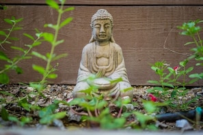 A stone Buddha statue in a garden setting with wooden background and surrounding greenery. - Firepit + Deck BBQ | Walk to Downtown Tasting Rooms | Vintage Paso (Paso Robles)