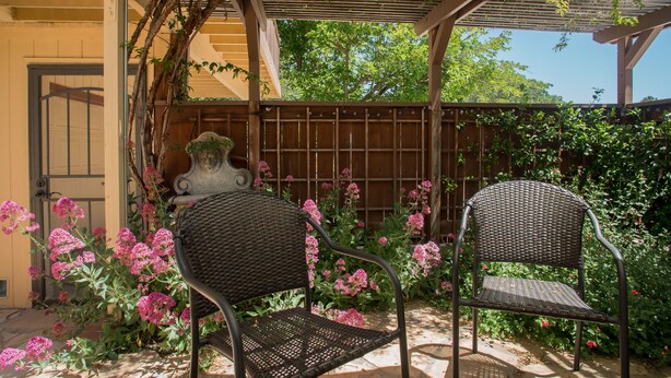 Une terrasse couverte avec deux fauteuils en osier, une clôture en bois et des plantes en fleurs.