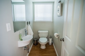 A small, clean bathroom with a white sink, mirror, toilet, and window blinds. - Firepit + Deck BBQ | Walk to Downtown Tasting Rooms | Vintage Paso (Paso Robles)