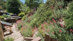 A garden with a wooden deck, a stone pathway, and various plants and flowers. - Firepit + Deck BBQ | Walk to Downtown Tasting Rooms | Vintage Paso (Paso Robles)