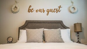 Un lit bien fait, avec une tête de lit, deux éléments décoratifs accrochés au mur, une lampe de chevet et une horloge.