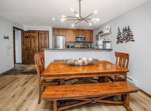 A dining area with a wooden table and benches, a kitchen with wooden cabinets and stainless steel appliances, and a decorative wall piece.
