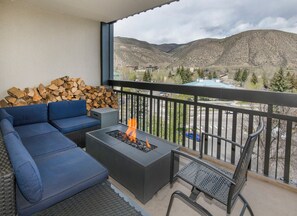 Un balcon avec un canapé, un foyer et un fauteuil, offrant une vue sur un paysage montagneux.